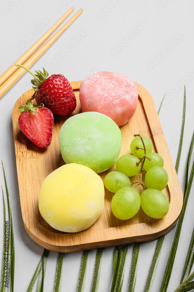 浅色背景下有美味的糯米团、水果和筷子的木板