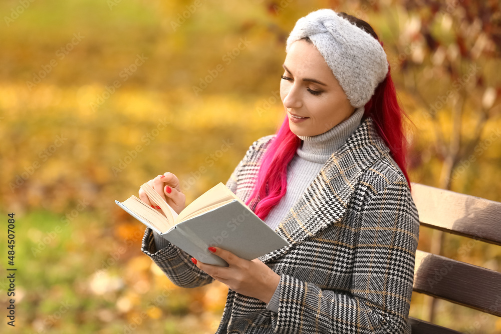 美丽的女人在秋天公园的长椅上看书