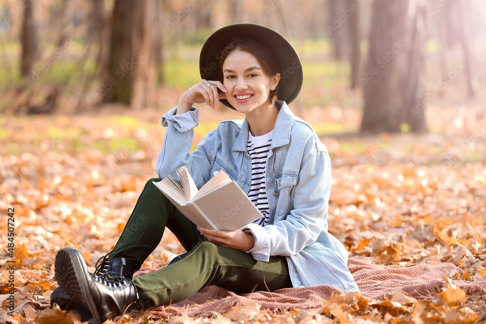 美丽微笑的女人，在秋天的公园里用格子布看书