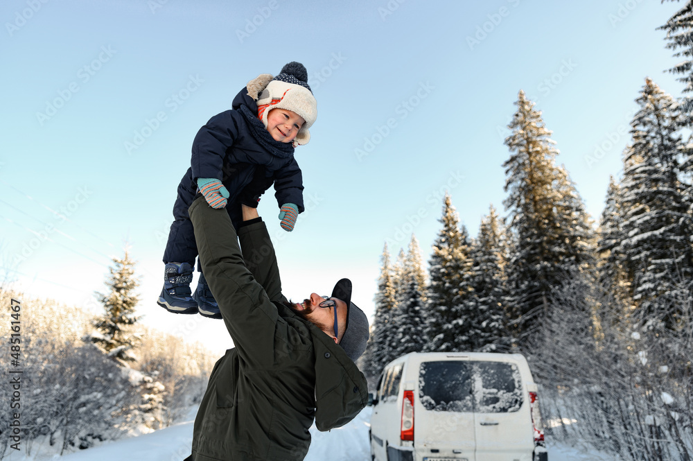 a father with a beard and glasses holds his little son in his arms on a winter walk against the back