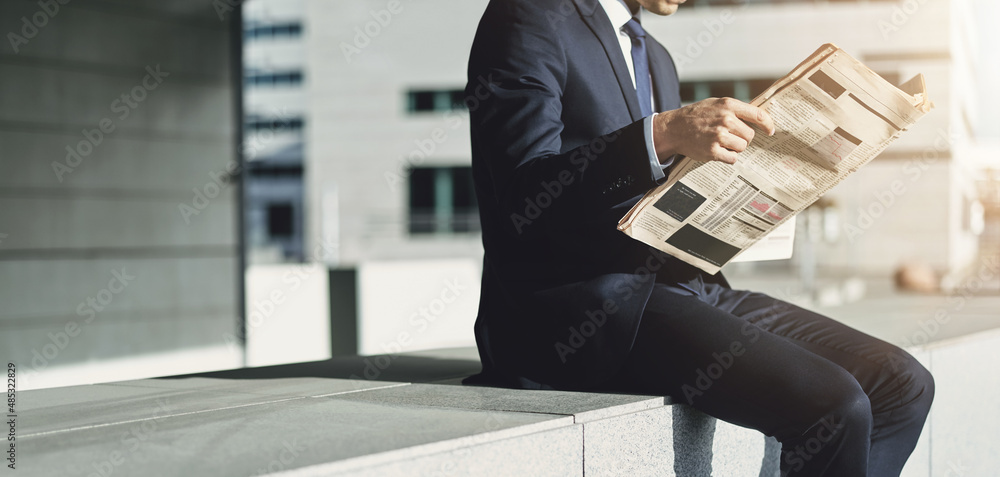 坐在办公楼外看财经报纸的商人