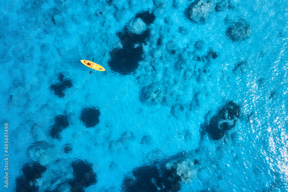 夏日日落时，蓝色大海中黄色皮划艇的鸟瞰图。清澈湛蓝的海水中漂浮着独木舟的男子