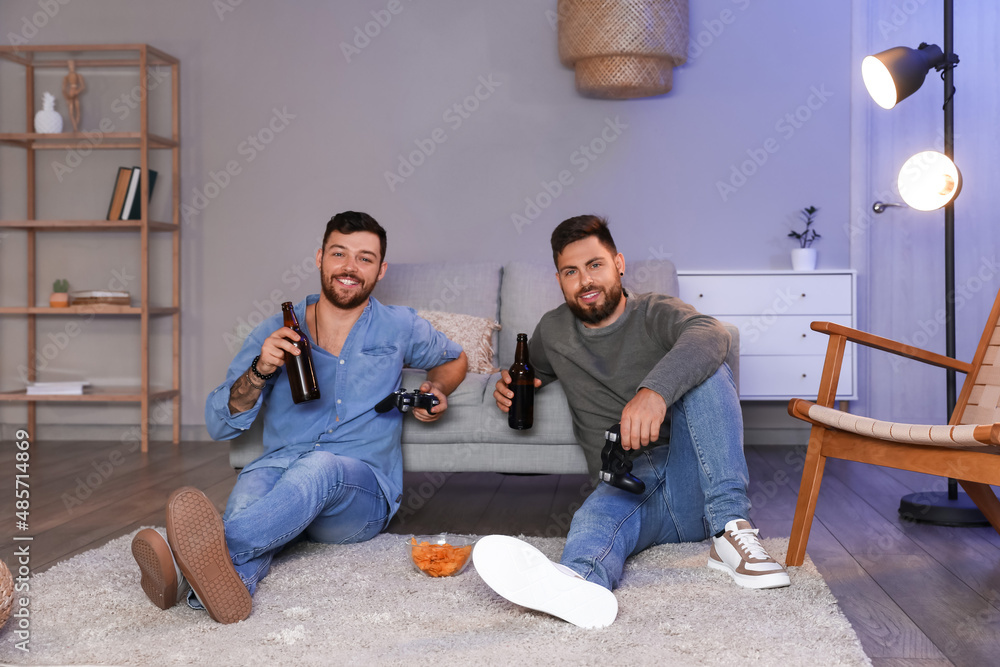 Young brothers with bottles of beer playing video game at home in evening