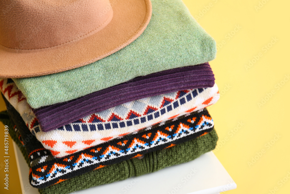 一堆时尚的毛衣和毡帽放在靠近彩色墙的椅子上，特写