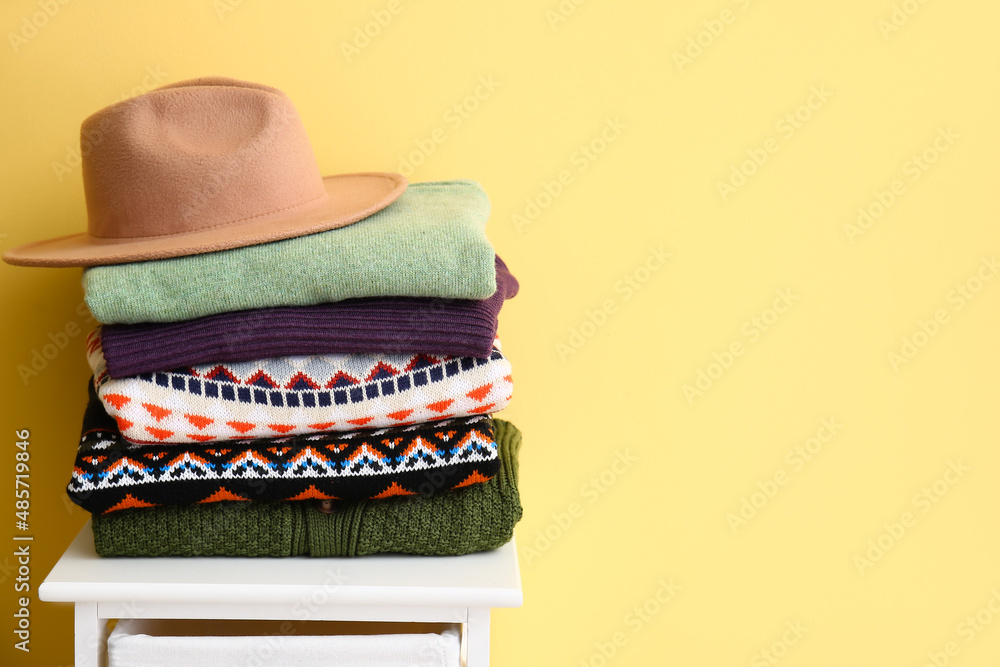 彩色墙附近凳子上一堆时尚的毛衣和毡帽