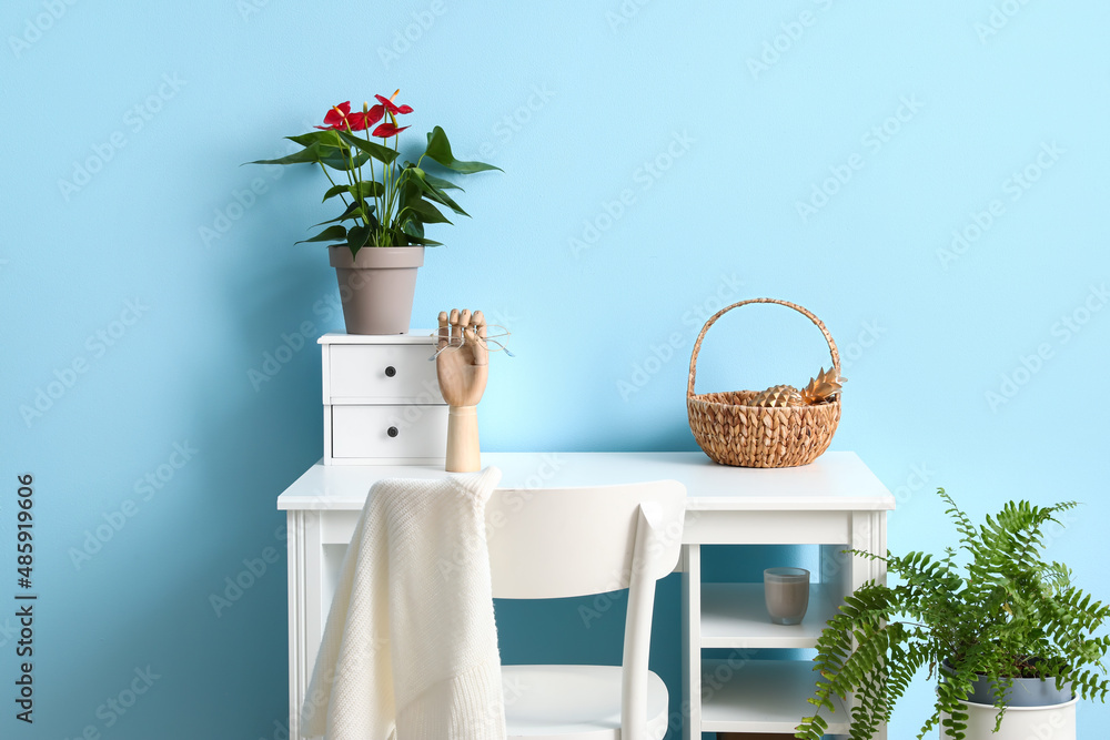 Workplace with Anthurium flower, wooden hand holding eyeglasses and basket on color background