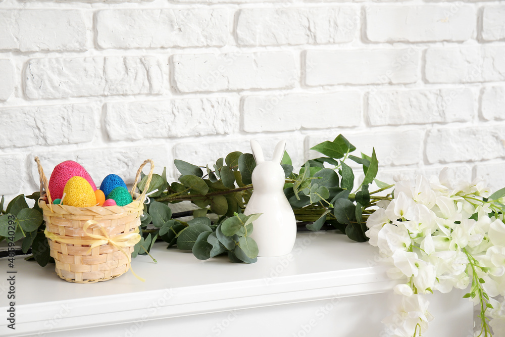 白色砖墙附近的壁炉台上有复活节彩蛋、装饰、桉树和鲜花的篮子