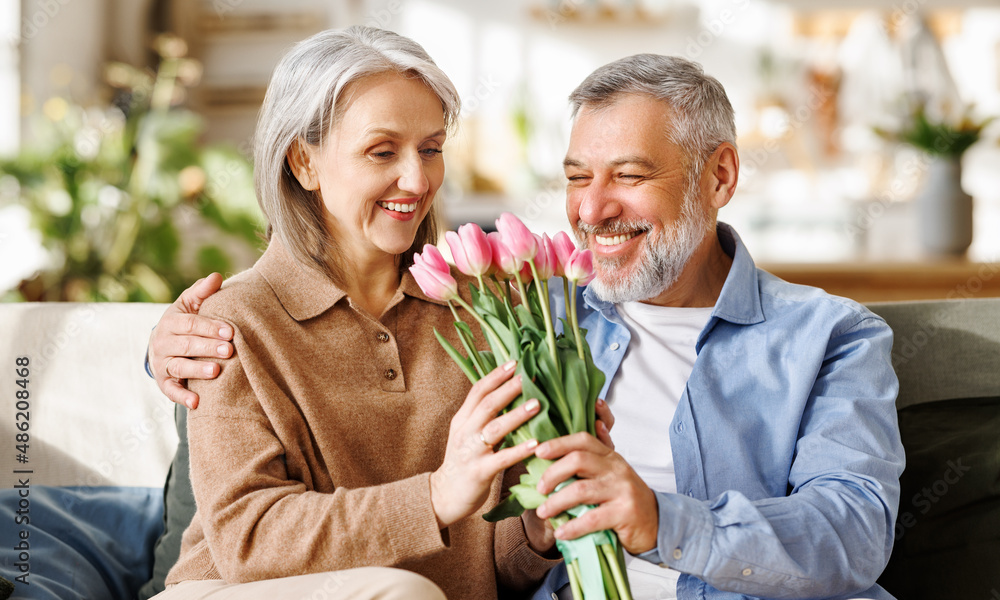 Happy senior woman getting romantic present bouquet of tulips from loving husband on Valentines Day