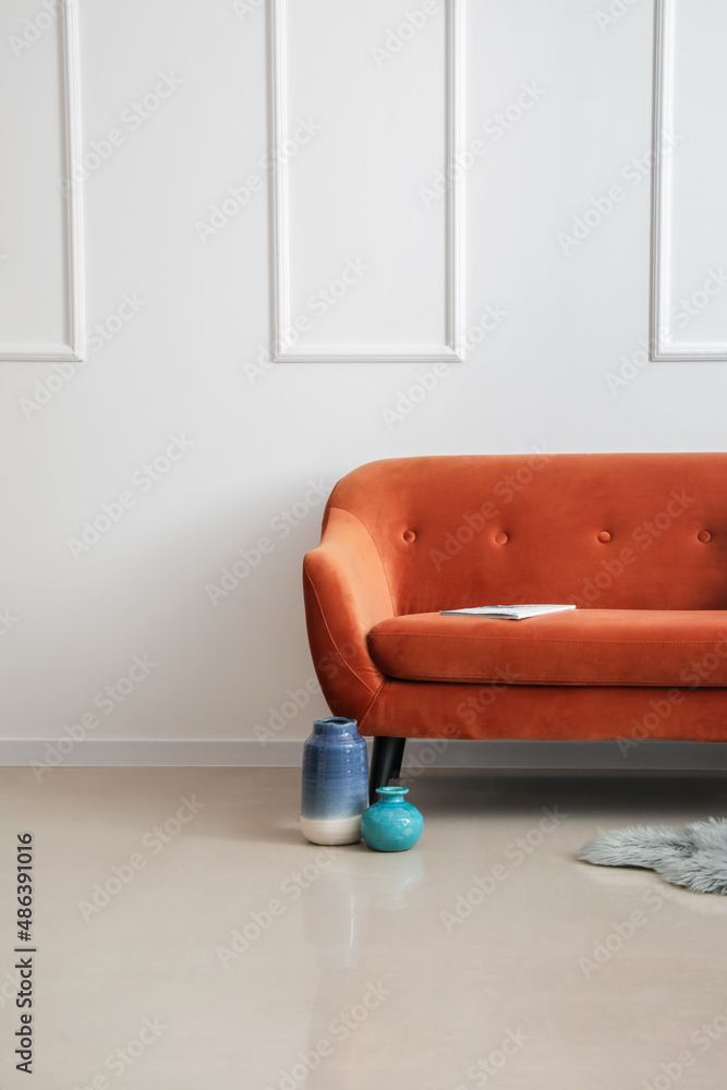 时尚的棕色沙发、花瓶和杂志靠近浅色墙壁