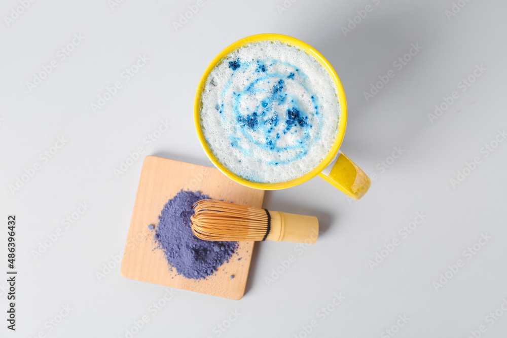 Cup of tasty blue matcha latte with chasen and powder on white background