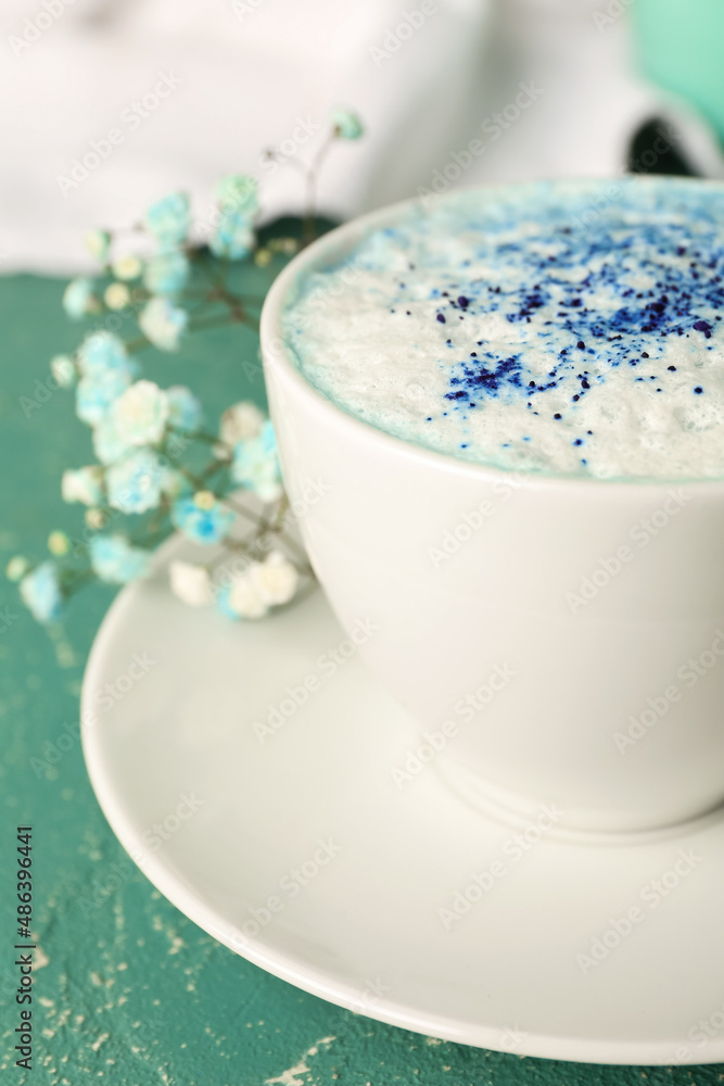 Cup of blue matcha latte and flowers on color background, closeup