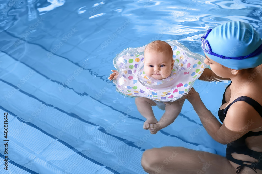 年轻的母亲和她可爱的婴儿在游泳池里带着充气环