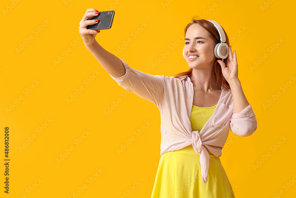 戴着耳机的年轻红发女子在黄色背景下自拍