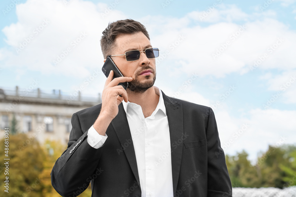 Stylish businessman in sunglasses talking by mobile phone on city square