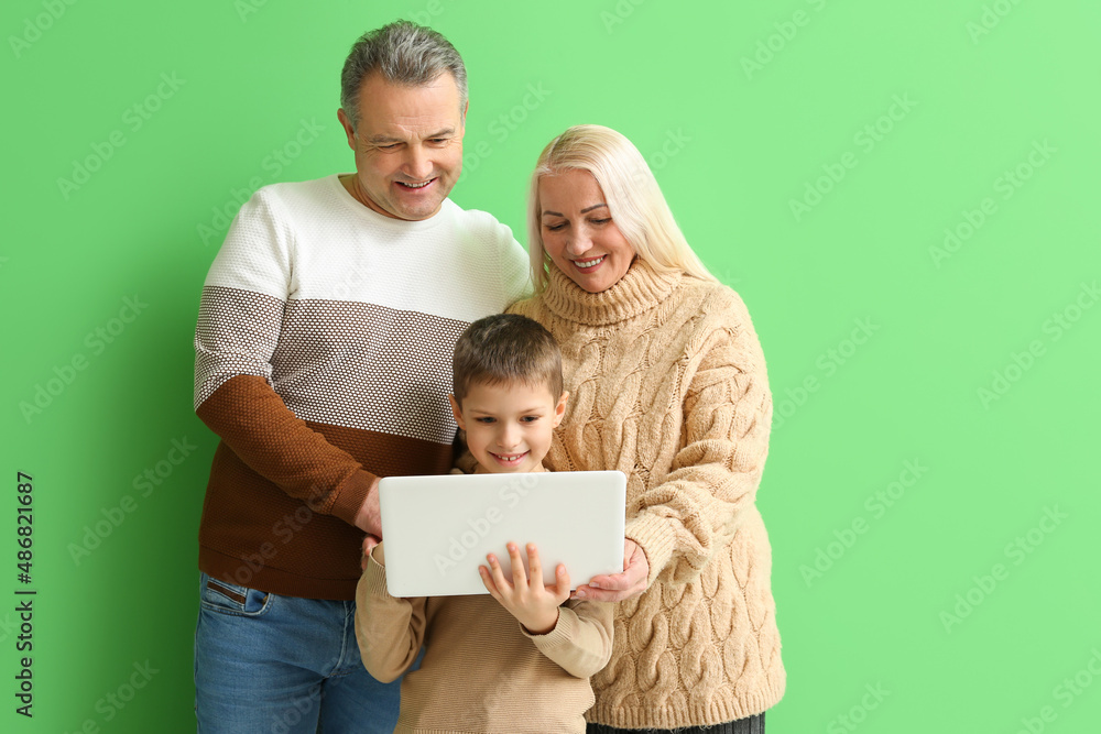 小男孩和爷爷奶奶穿着暖和的毛衣，在绿色背景下使用笔记本电脑