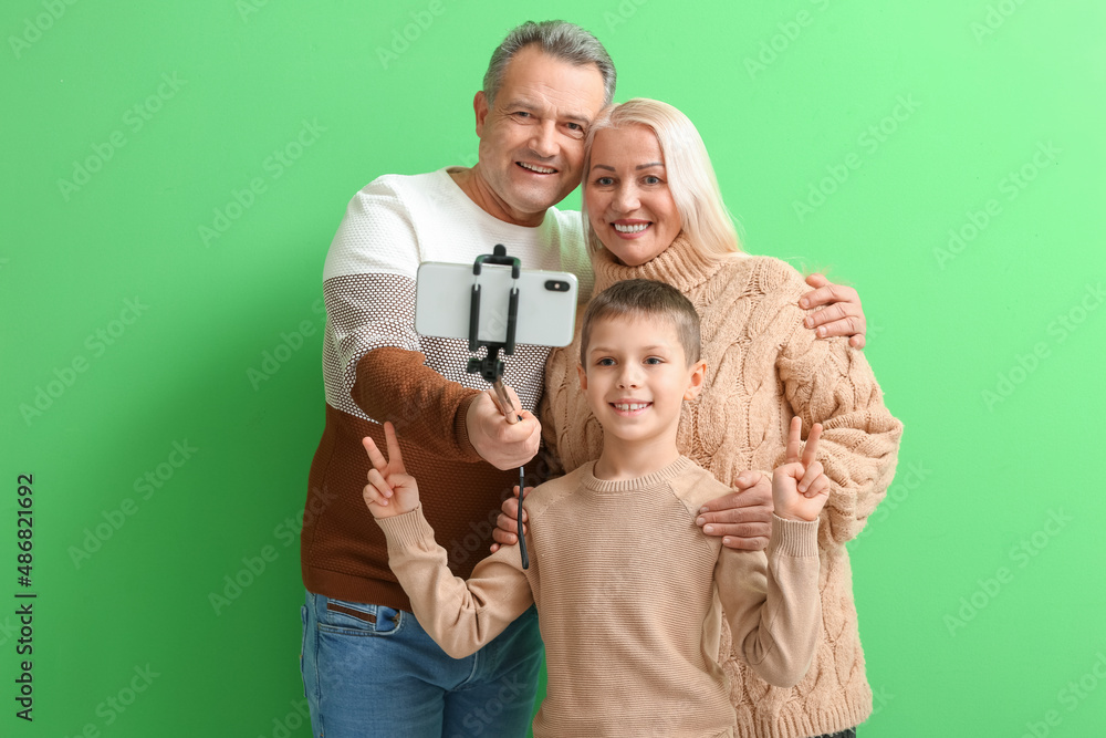 Little boy with his grandparents in warm sweaters taking selfie on green background