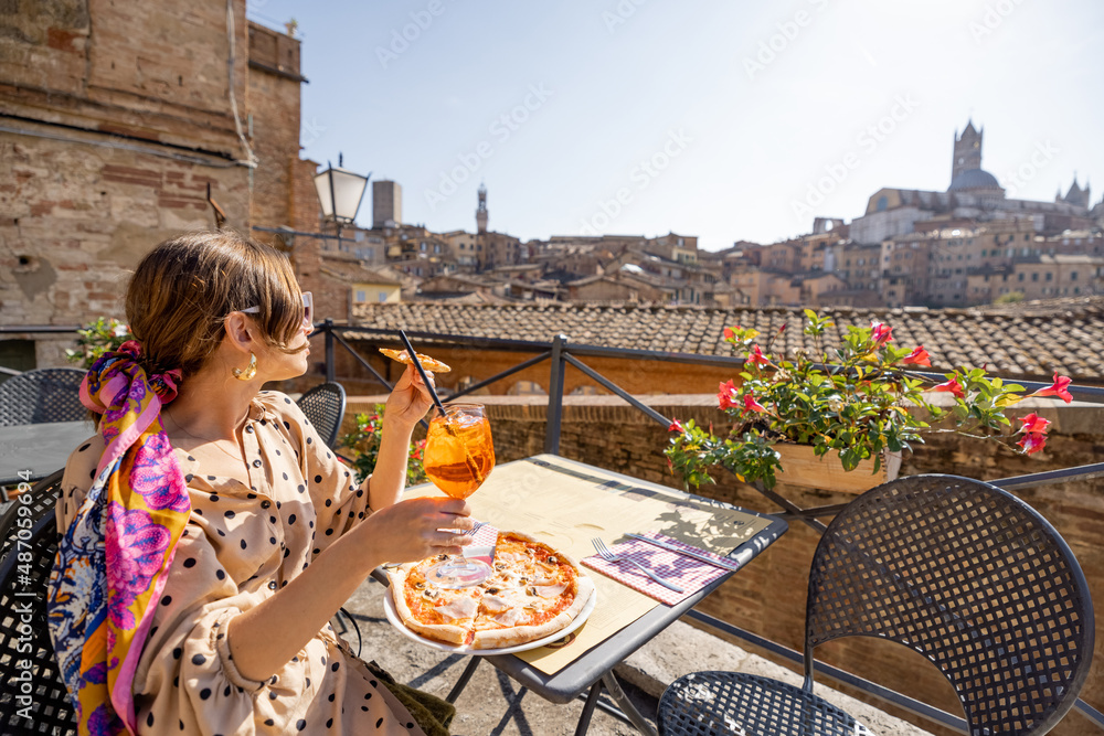 Young woman having lunch with pizza and wine at outdoor restaurant with beautiful view on the old to