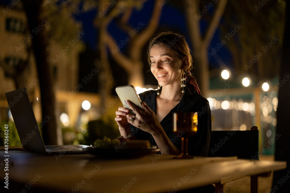 高加索女人晚上在户外用笔记本电脑和手机看东西。年轻女人坐着