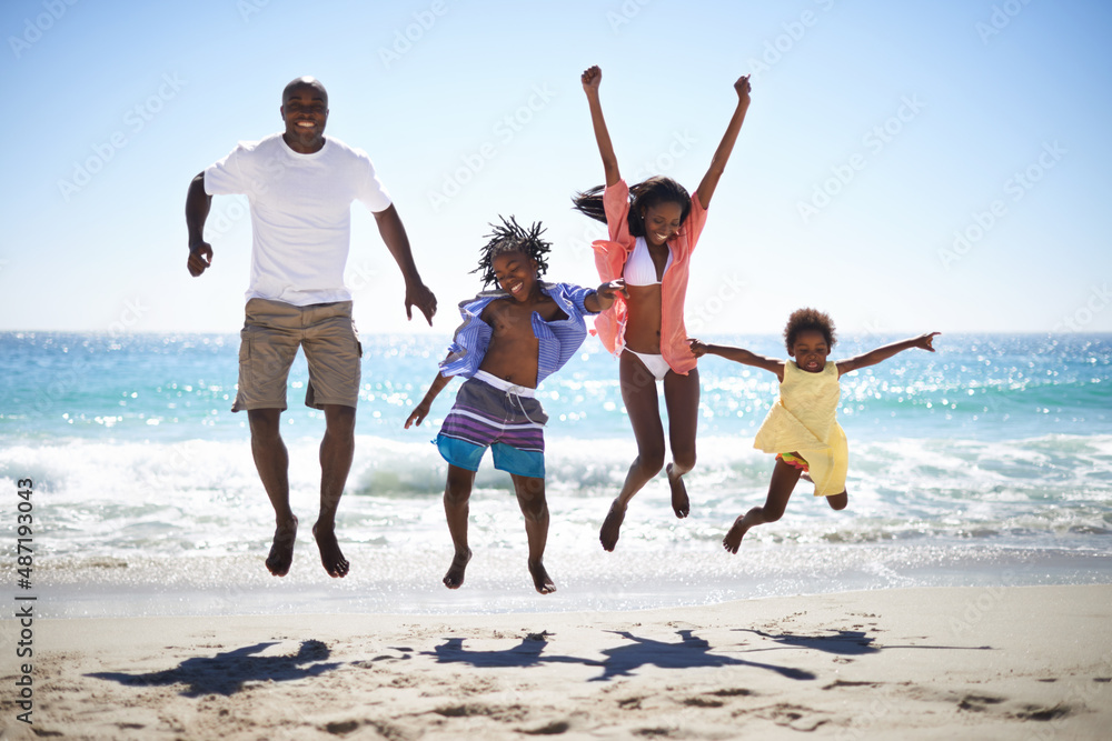 哇喔度假时间太棒了。一个兴奋的非裔美国人家庭在海滩上跳到空中。