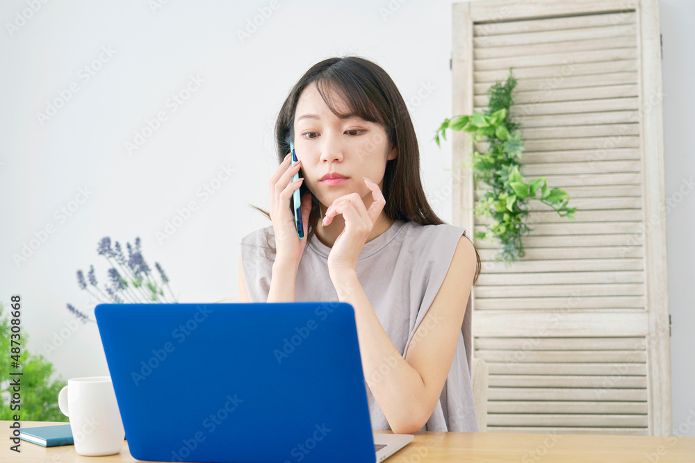 女性　パソコンを使いながら電話する　リビング