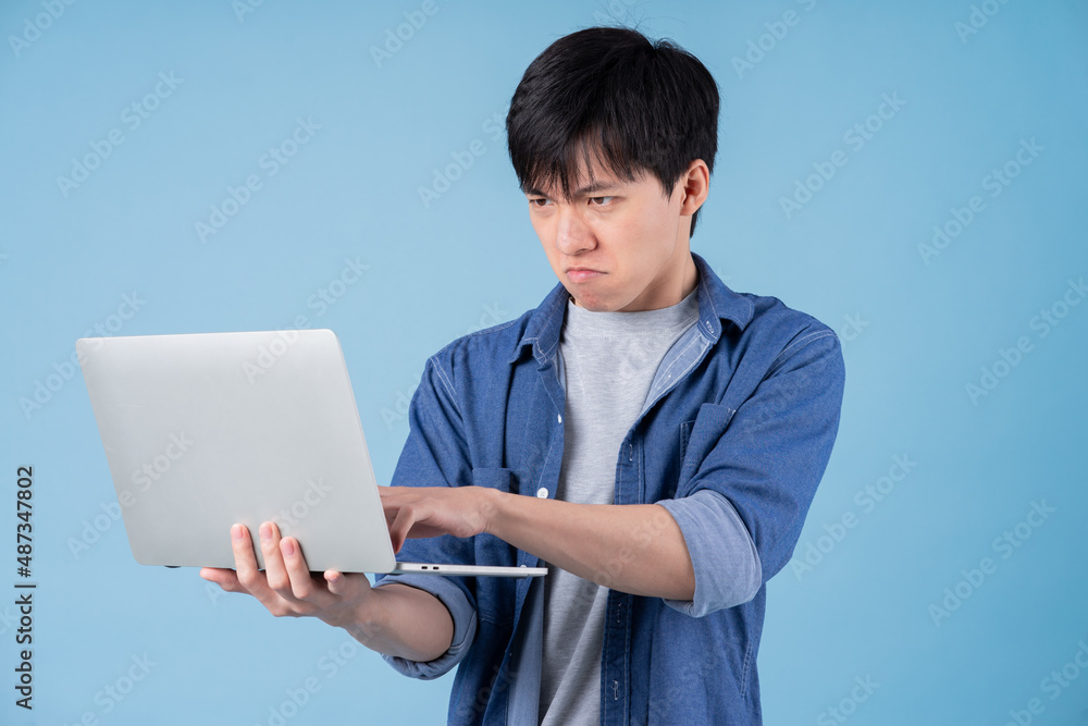年轻的亚洲男子在蓝色背景下使用笔记本电脑