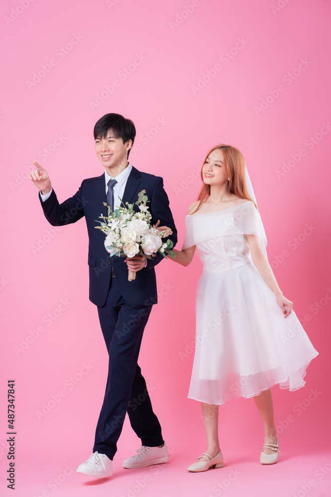 年轻的亚洲新娘和新郎在粉色背景下摆姿势