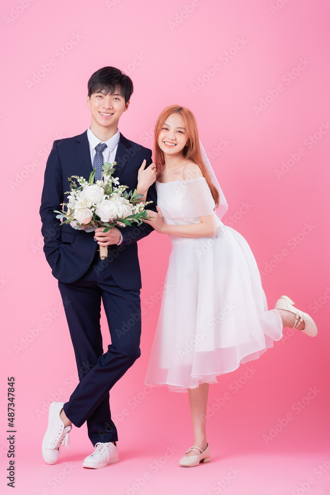 年轻的亚洲新娘和新郎在粉色背景下摆姿势