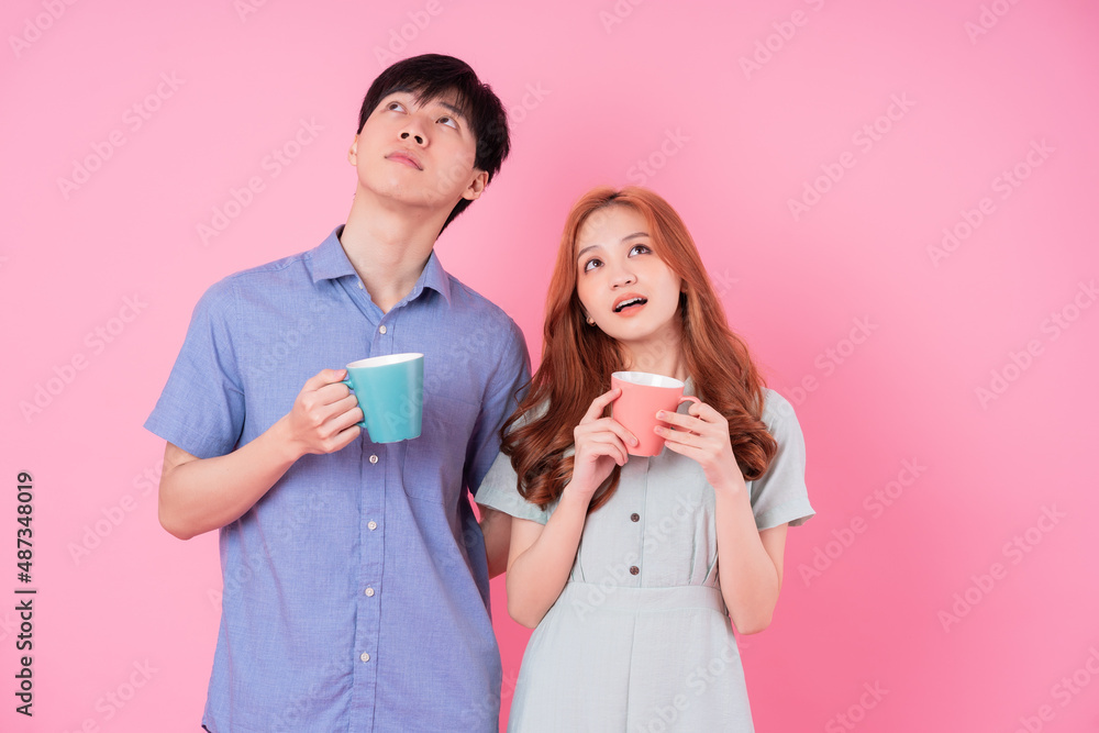 年轻的亚洲夫妇在粉红色的背景下喝茶