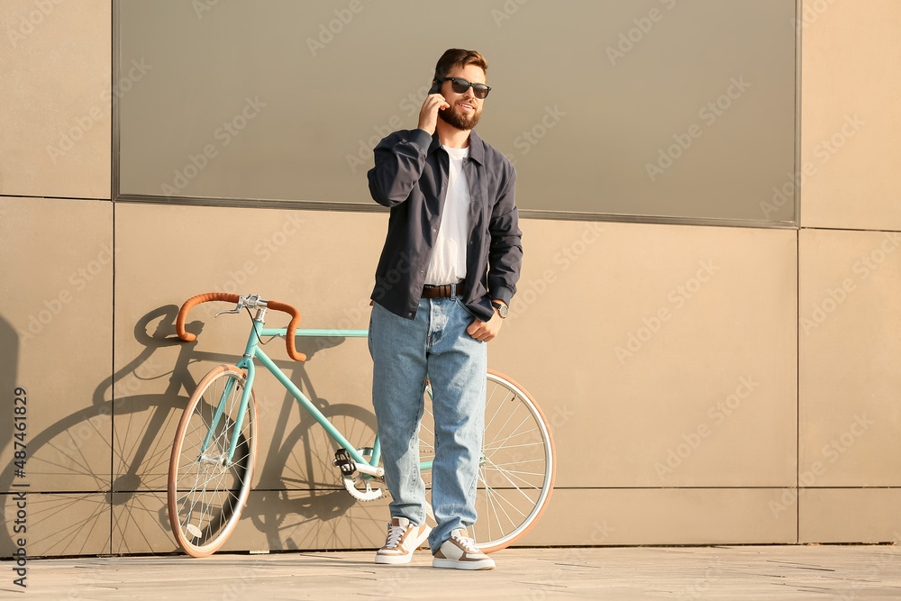 时髦的大胡子男子骑着自行车在城市里用手机聊天