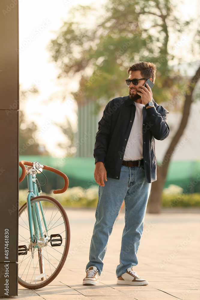 时髦的大胡子男子骑着自行车在城市里打手机
