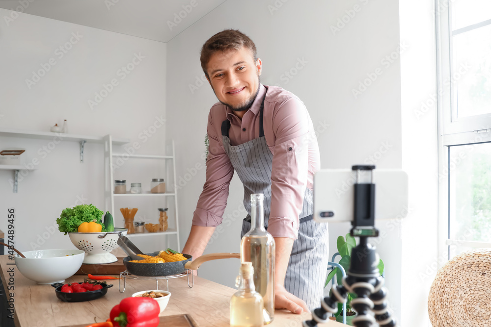 Young man recording cooking video tutorial on mobile phone in kitchen
