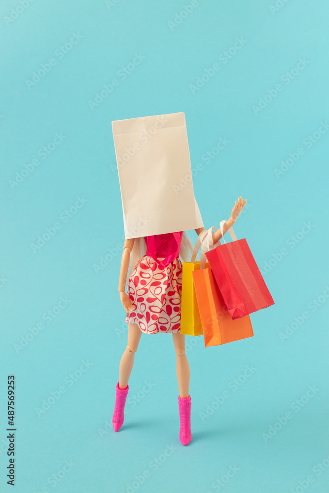 时尚女孩的创意造型，头上戴着白色纸袋，在淡蓝色ba上拿着彩色袋子