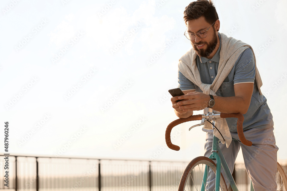 年轻的大胡子男子骑着自行车在路堤上用手机