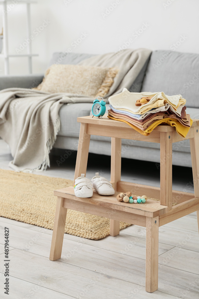 Stepladder stool with baby clothes, shoes and alarm clock in room