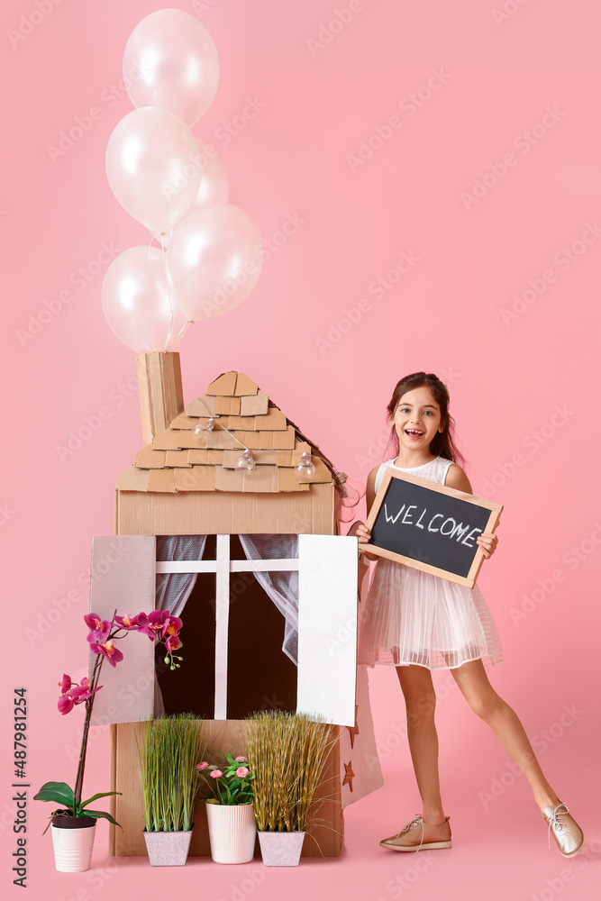 有趣的小女孩在粉色背景下玩纸板房子