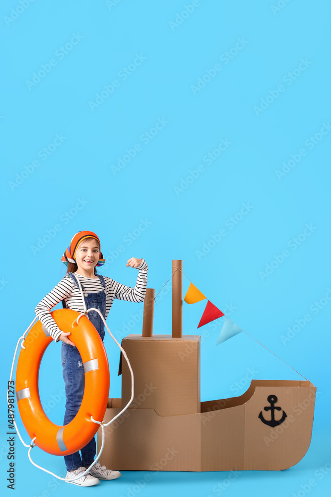 有趣的小女孩在蓝色背景下玩纸板船