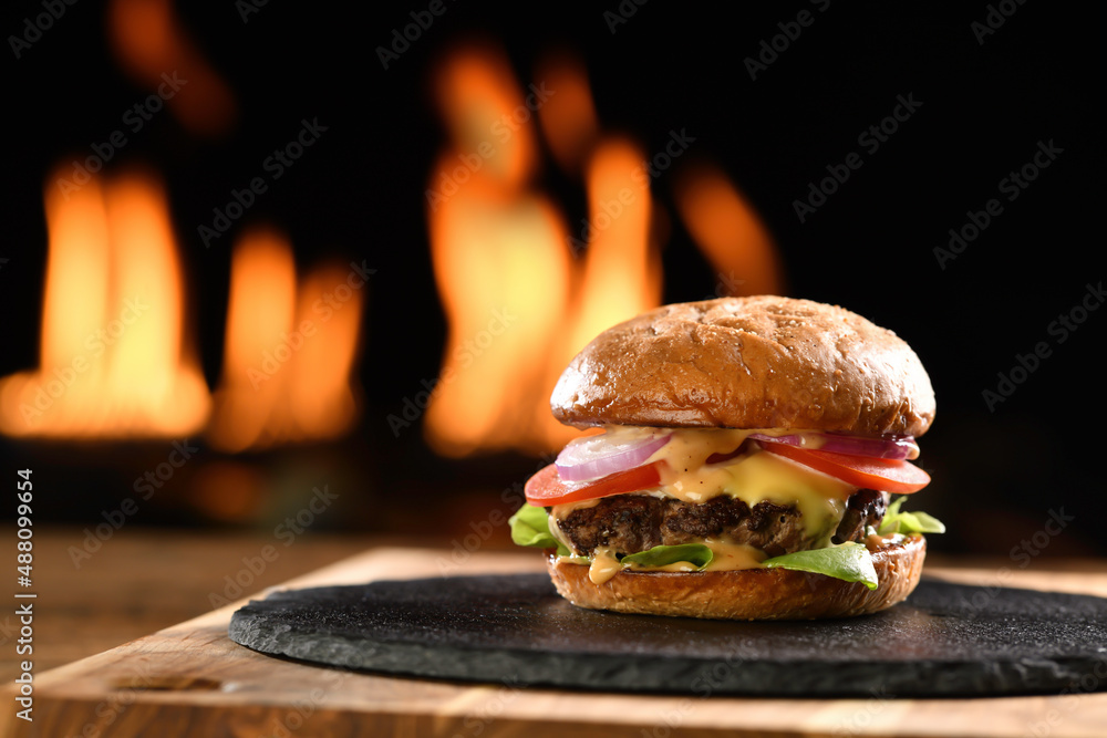 Meat cheeseburger with vegetables on black plate with flaming background.