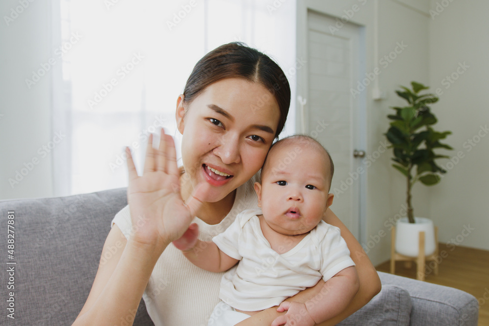 观点，年轻的亚洲母亲和她的新生儿微笑着通过视频通话打招呼/道别