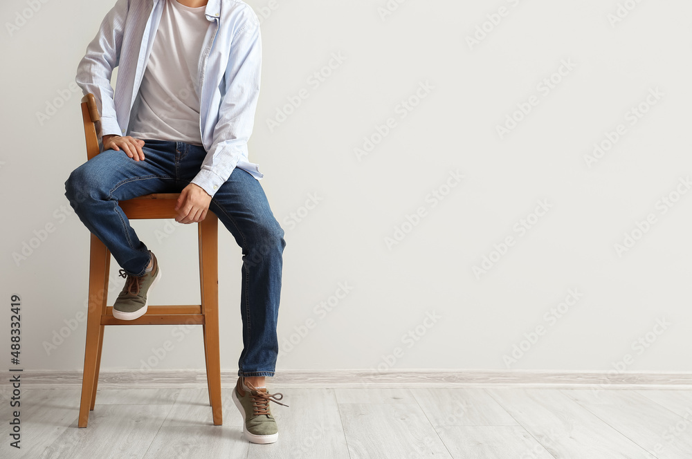 穿着时尚牛仔裤的时尚年轻人坐在灯光墙附近的椅子上