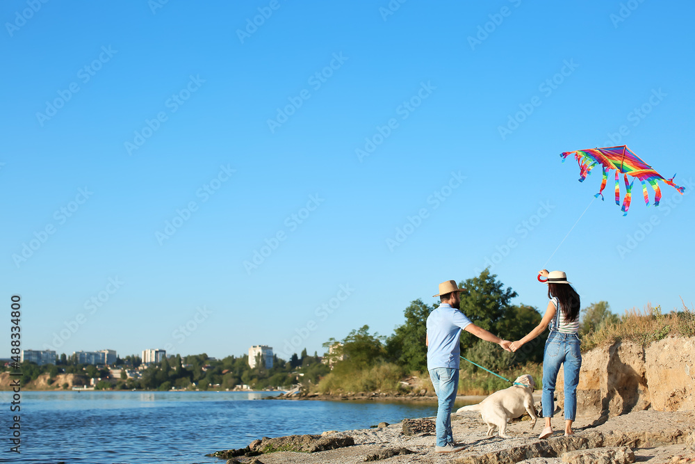 快乐的年轻夫妇和可爱的小狗在河边放风筝