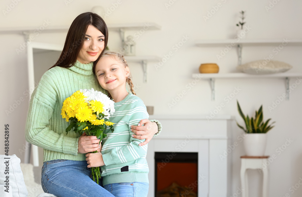 Young mother and her little daughter in sweaters with flowers at home