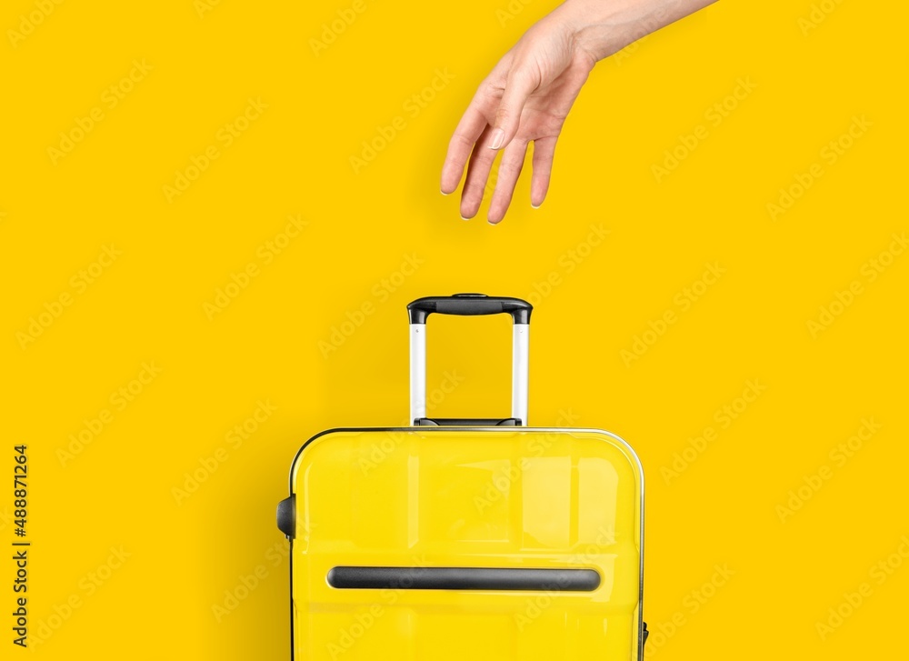 女性手拿着亮黄色背景的行李箱
