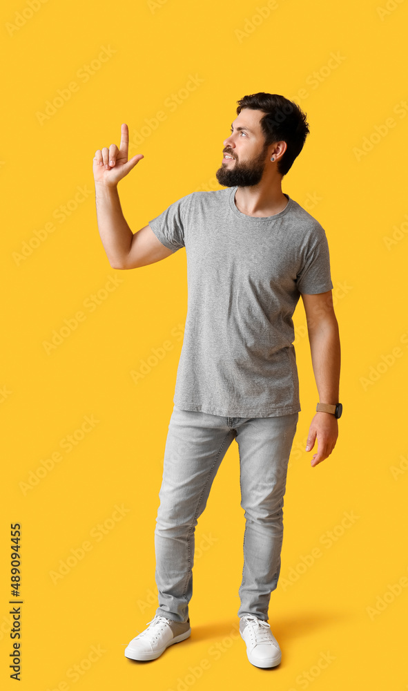 Handsome man in grey t-shirt pointing at something on yellow background