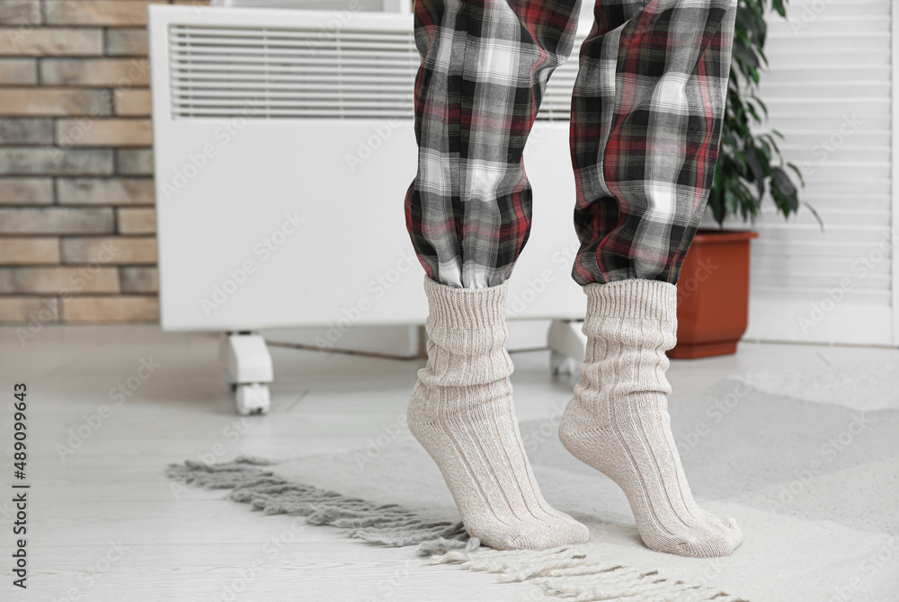 家里电加热器附近穿着保暖针织袜的女人。供暖季节的概念