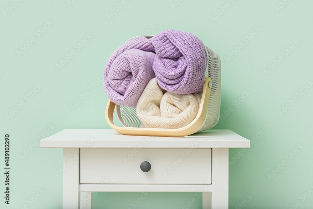 Basket with rolled sweaters on table near color wall