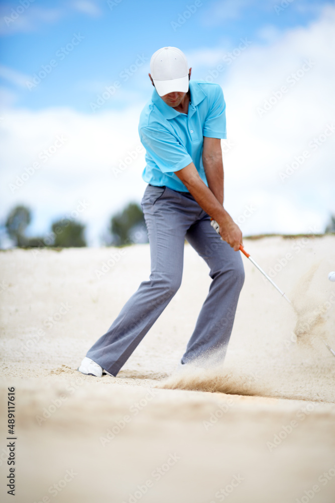 在沙坑里。一张年轻男子高尔夫球手在高尔夫比赛中将球从沙坑中铲出的照片。