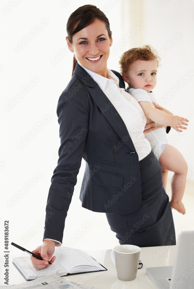 Work meets motherhood..and shes got it covered. Working mother holding her baby while smiling and si