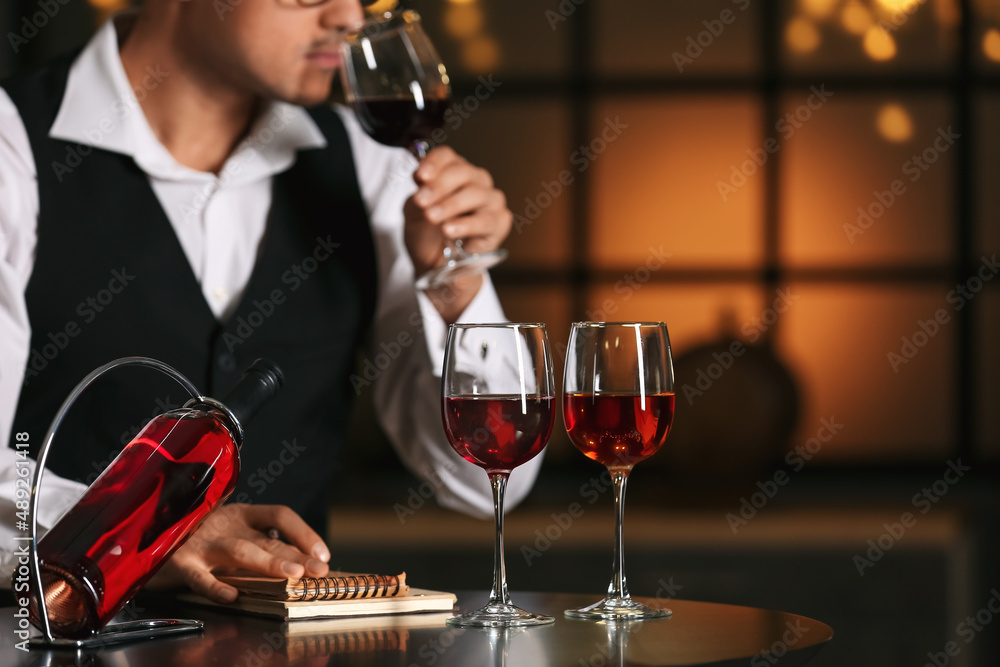 年轻男性侍酒师品尝葡萄酒类型，专注于酒瓶和玻璃杯