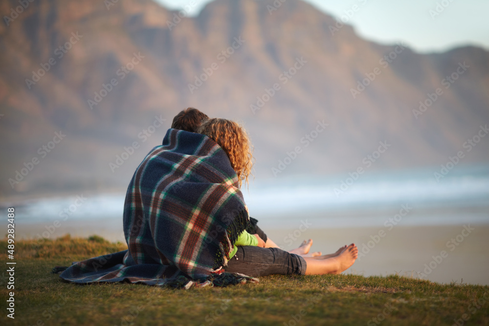 欣赏美景。一对可爱的年轻夫妇坐在河岸上，裹着毯子。
