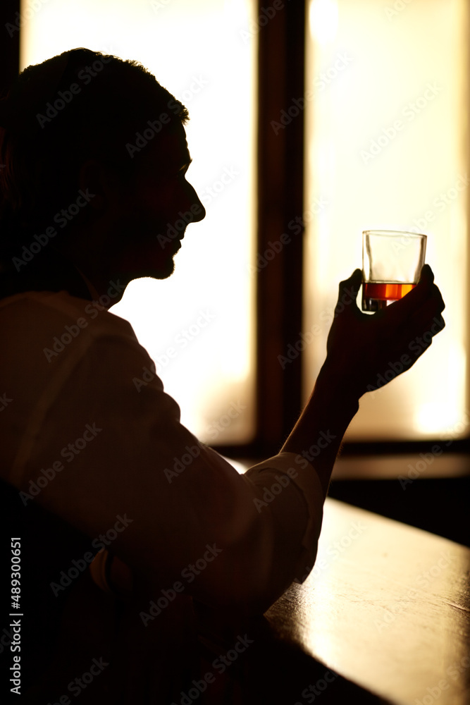 Sitting in quiet contemplation. Profile silhouette of a young man sitting at a bar and holding up a 